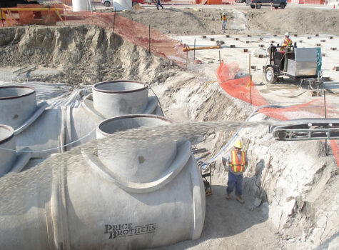 Worker watching as gravel truck throws backfill into a hole