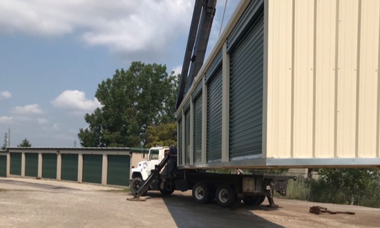 Truck with crane moving a large storage unit into place.